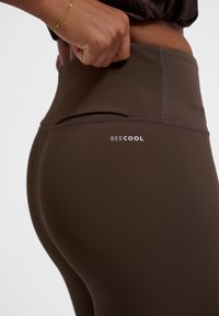 Bruna högmidjade leggings med en slät textur. Har en BEECOOL-logotyp på baksidan, med flata sömmar som ökar hållbarheten.