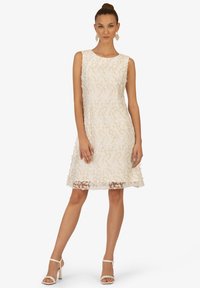 Beige ärmelloses Kleid mit aufwändiger floraler Stickerei, ausgestellter A-Linie, knielang, mit transparentem Saum, ergänzt durch Riemchenhighheels.