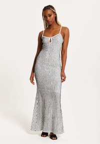 Long, form-fitting dress in black and white with vertical stripe pattern. Features spaghettis straps and a keyhole neckline detail.