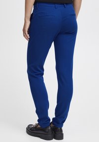Blaue, eng anliegende Hosen aus glattem Stoff, mit einer Gesäßtasche und einem eleganten Design. Getragen mit schwarzen Slippern.