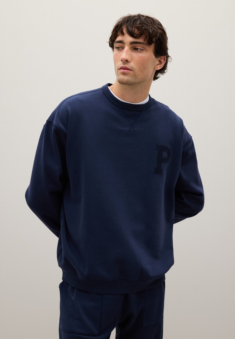Sudadera azul marino de material suave con un logo texturizado de la 'P' en el pecho. Presenta un cuello redondo y un corte relajado.