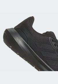 Chaussure de course noire légère avec une tige en tissu texturé, une semelle amortie et trois bandes parallèles sur le côté.