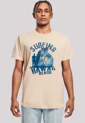 Beige Baumwoll-T-Shirt mit einem blauen Grafikdruck eines Surfers, Palmen und dem Text "Surfing Hawaii Beach". Kurze Ärmel, Rundhals-Design.