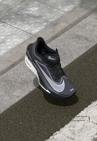 Chaussure de course Nike Zoom Fly en noir et gris. Caractéristiques : tige en maille avec perforations, design épuré et semelle blanche ZoomX pour un meilleur amorti.
