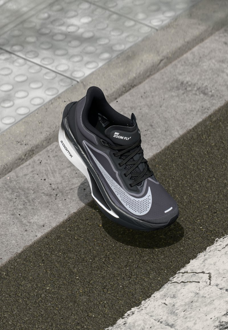 Chaussure de course Nike Zoom Fly en noir et gris. Caractéristiques : tige en maille avec perforations, design épuré et semelle blanche ZoomX pour un meilleur amorti.