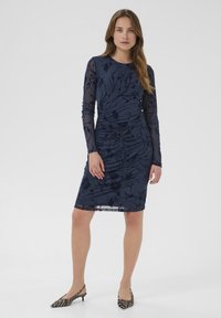 Tengeri ruha virágmintával, hosszú áttetsző ujjak, ráncos kialakítás, térdig érő hossz. Fekete és fehér csíkozott sling-back magassarkúval párosítva.