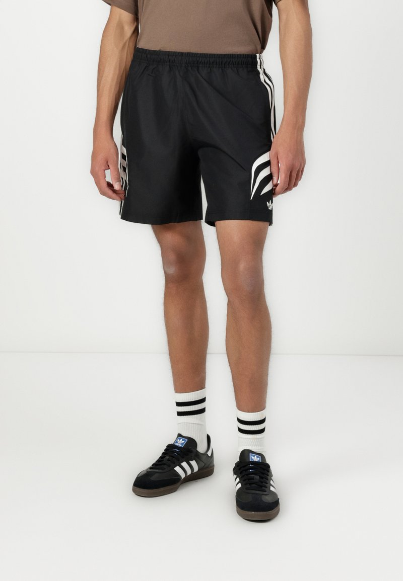 Sorte atletiske shorts med en glat tekstur, elastisk talje, og hvide sidestreger. Parret med sorte sneakers og stribede sokker.