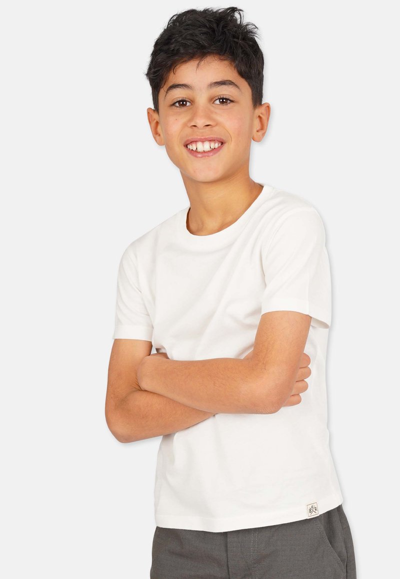 Hvid bomulds T-shirt med korte ærmer, rund halsudskæring og et lille logomærke ved kanten, kombineret med grå bukser. Glat tekstur.