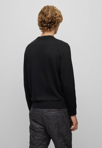 Zwarte trui met een ronde hals, lange mouwen en een zachte textuur, gecombineerd met donkergrauwe gewatteerde broeken met een subtiel patroon.