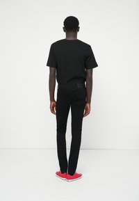 Tricou negru cu mânecă scurtă, accesorizat cu blugi negri ajustați și adidași roșii. Tricoul are un guler clasic rotund și o textură a materialului neted.