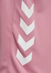 Ljust rosa tyg med vita chevronmönster. Materialet verkar slätt med en lätt lyster och visar en modern design.