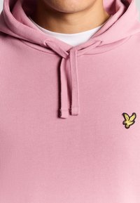 Felpa con cappuccio rosa chiaro dotata di coulisse regolabile. Piccolo logo giallo ricamato sul lato sinistro del petto. Tessuto morbido e dalle texture piacevoli.