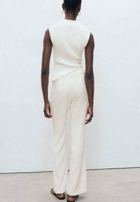 Top bianco a coste senza maniche abbinato a pantaloni a vita alta e gamba affusolata. Il tessuto è liscio con una texture morbida. Design semplice con accenti minimi.