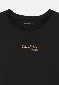 Juodas medvilnės marškinėliai su apvalia pašiuoste ir mažuoju auksiniu logotipu "Calvin Klein New York", išsiuvinėtu ant kairiojo krūtinės kampo.
