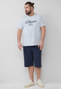 T-shirt en coton bleu clair avec texte bleu marine, assortie à un short bleu marine jusqu'aux genoux. Des baskets blanches complètent la tenue. Design simple et décontracté.