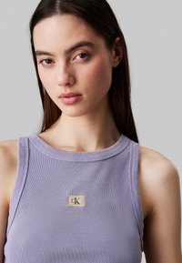 Top senza maniche viola a coste con scollatura rotonda. Presenta un piccolo etichetta di marca al centro. Tessuto morbido con una superficie liscia.