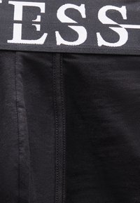 Κοντινή λήψη μαύρου υφάσματος με μια ζώνη μέσης που φέρει μεγάλα λευκά γράμματα «ESS» σε σκούρο φόντο.