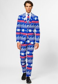 Traje azul brillante con copos de nieve blancos, rayas rojas y blancas, y patrones de renos, combinado con una corbata a juego y zapatos negros.