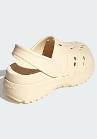 Sabot en mousse beige avec une arrière fermé, des trous de ventilation sur le côté, une surface texturée et une semelle texturée pour une meilleure adhérence. Comprend une sangle de talon flexible.
