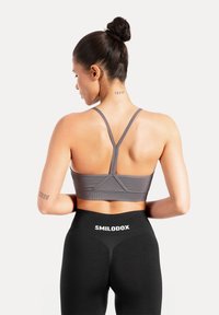 Grijze sportbeha met smalle bandjes, een strak ontwerp en een racerback-stijl. Zwarte leggings met een wit "SMILODOX"-logo op de tailleband.