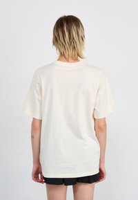 Crème-kleurige katoenen t-shirt met een relaxte pasvorm, korte mouwen en een ronde halslijn; eenvoudige achterkant met minimale stikdetails.