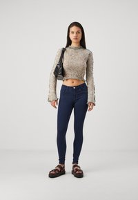 Häkel-Strickpullover in Multicolor mit rüschierten Kanten, kombiniert mit dunkelblauen Skinny Jeans und klobigen braunen Sandalen. Schwarze Schultertasche.