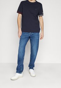 Námořnické tričko s červenými a modrými pruhovanými akcenty na rukávech, doplněné modrými džíny a bílými teniskami. Jednoduchý, ležérní design.