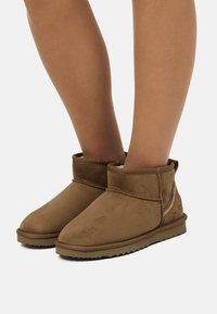 Bottes chelsea en suède marron, avec un bout arrondi, une texture douce, peu de coutures et une semelle en caoutchouc à profil bas.