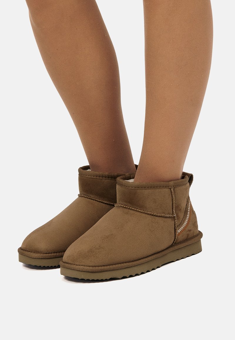 Bottes chelsea en suède marron, avec un bout arrondi, une texture douce, peu de coutures et une semelle en caoutchouc à profil bas.