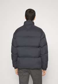 Czarna pikowana kurtka puchowa z wysokim kołnierzem, pikowanym wzorem i zaokrąglonymi ramionami. Teksturowana tkanina zapewnia izolację i ciepło.