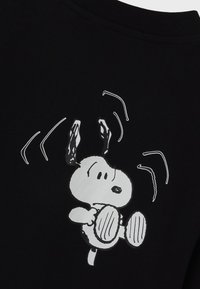 Sudadera negra con un perro de dibujos animados con orejas largas, en blanco, representado en una pose juguetona con líneas onduladas sobre su cabeza.