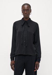 Svart langermet skjorte med krage og knepping i front. Glatt stoff, løs passform, med en litt blank tekstur og minimale detaljer.