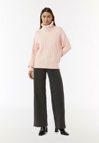 Chunky rosa Kabelstrick-Turtleneck-Pullover mit gerippten Bündchen, kombiniert mit hoch taillierten, dunkelgrauen, weit geschnittenen Jeans und schwarzen, hochhackigen Stiefeletten.