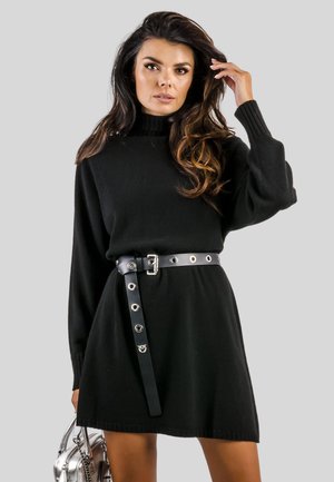 Abito in maglia nera con colletto alto, maniche lunghe e vita aderente accentuata da una cintura nera con occhielli argentati e fibbia.