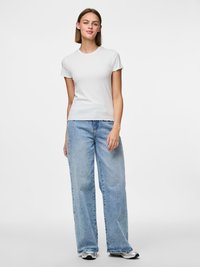 Bílé žebrované tričko s krátkým rukávem a vlnitým lemem, spojené s volnými světle modrými džíny. Zobrazeno na neutrálním pozadí.