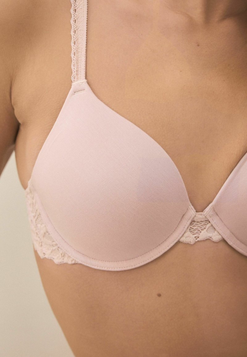 Bra imbottito rosa con tessuto liscio e dettagli in pizzo lungo il sottobande. Spalline regolabili con una finitura testurizzata. Forma del coppa triangolare.
