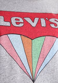 T-shirt grafica grigia con logo rosso "Levi's" e un disegno di cuore colorato con sezioni rosa, arancione, verde e blu.
