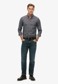 Mørkeblå skjorte med knapper, denim jeans, sort bælte og lædersko. Slim fit, lange ærmer oprullet, og ur på håndleddet.
