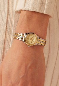 Gouden en zilveren metalen horloge met een ronde, gouden wijzerplaat, voorzien van uurmarkeringen en een datumaanduiding, bevestigd aan een schakelarmband.