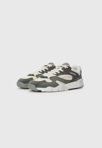 Lacoste sneakers feature a mix of gray and off-white materials, with perforated details, red accents, and a textured rubber sole.