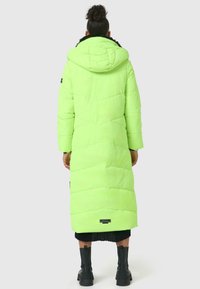 Neon groene lange pufferjas met een capuchon, gewatteerd ontwerp en zwarte details aan de zoom, gecombineerd met zwarte enkellaarsjes.