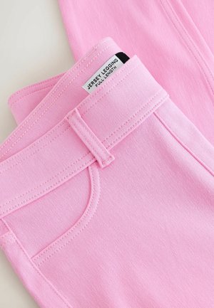 Gros plan sur un legging en jersey rose plié, longueur totale, montrant la boucle de ceinture, la poche avant et l'étiquette.