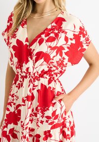 Short-sleeve dress in cream fabric with large red floral print, v-neckline, elastic waistband, and side pockets.