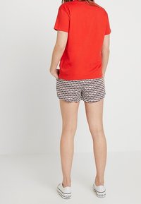 T-shirt in cotone rosso abbinato a pantaloni corti a fantasia in bianco, nero e rosso. Design semplice, vestibilità comoda e sneakers bianche.