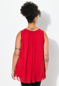 Top rosso senza maniche con una vestibilità ampia, realizzato in tessuto leggero, con dettaglio arricciato sul collo e una texture leggermente trasparente.