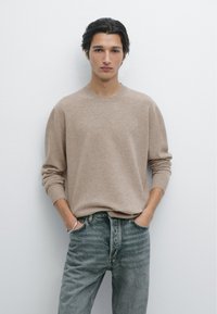 Beżowy sweter dzianinowy z okrągłym dekoltem, luźny krój i długie rękawy, w połączeniu z wyblakłymi niebieskimi dżinsami. Minimalistyczny design i faktura.