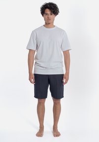 Jasnoszara bawełniana koszulka z krótkimi rękawami, zestawiona z ciemnogranatowymi szortami. Materiał wydaje się miękki, ma luźny krój i minimalne detale wzornicze.