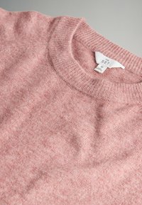 Roza pletena jopica s okroglim izrezom, mehka tekstura in oznaka "THE SET", velikost M. Ima rahlo marmorirano površino.