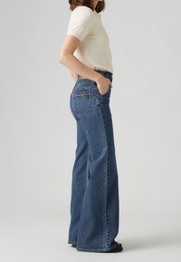 Vidjejeans i mörkblått med hög midja, synliga sömmar och två bakfickor. Strukturert tyg, sitter tight vid midjan och är lösa genom benen.