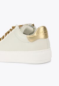 Sneaker bianco in pelle con accenti dorati, caratterizzato da un tab laterale in oro testurizzato e dettagli a catena lungo il lato, suola in gomma bianca.